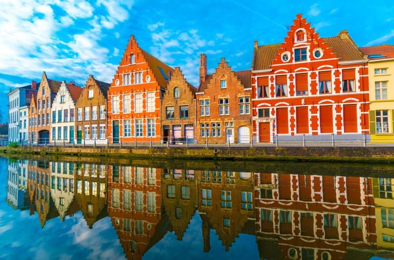 Colourful medieval buildings line a canal in Bruges and are reflected in the water